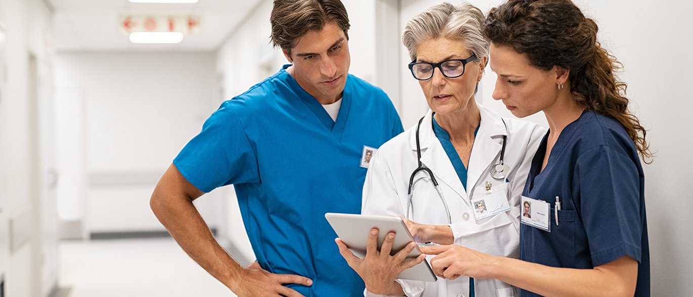 Læger og sygeplejersker kigger på tablet sammen på hospitalsgang